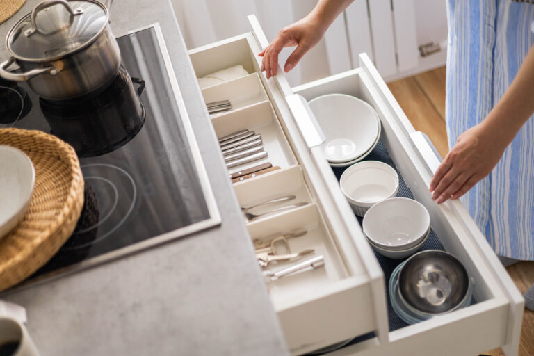 Top view modern housewife tidying up kitchen cupboard during general cleaning or tidying up. Female neatly placing dishware and cutlery in drawer of table. Storage organization Konmati method