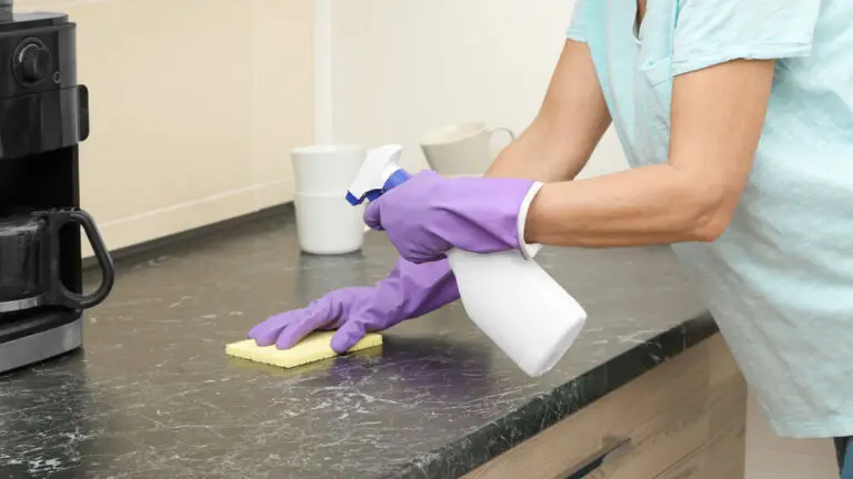 Professional deep cleaning services scrubbing a dark granite kitchen countertop with purple gloves and a spray bottle.