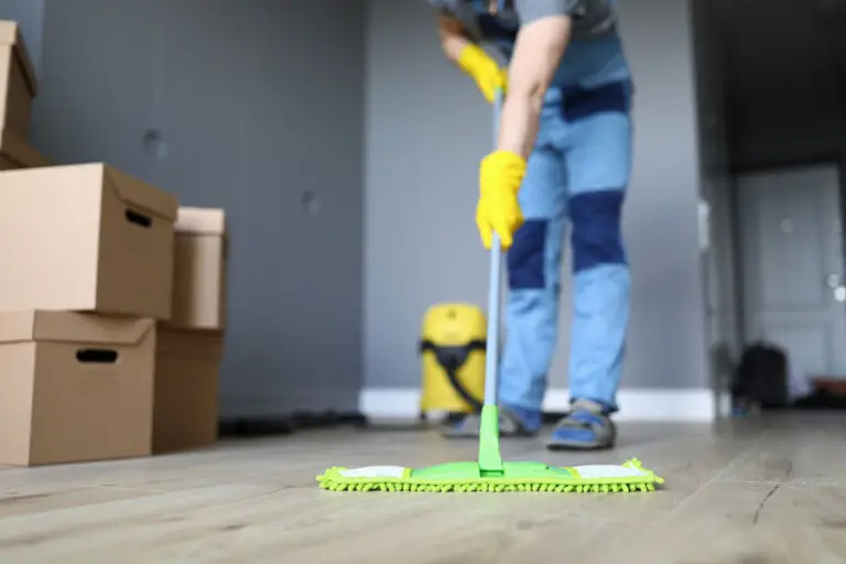 Professional cleaner in blue overalls mopping hardwood floors next to stacked boxes during a Move-Out Cleaning service.