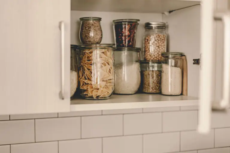 Pantry Organization: Glass jars filled with pasta, grains, and legumes neatly arranged on a shelf inside a white kitchen cabinet.