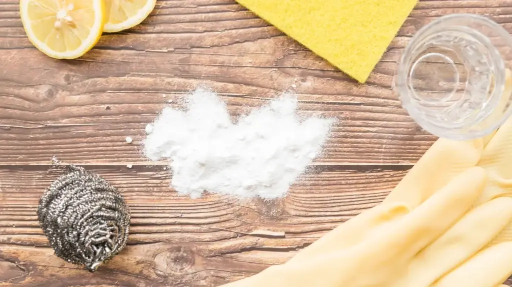 Natural cleaning supplies including lemon, baking soda, sponge, and gloves arranged on a wooden surface.